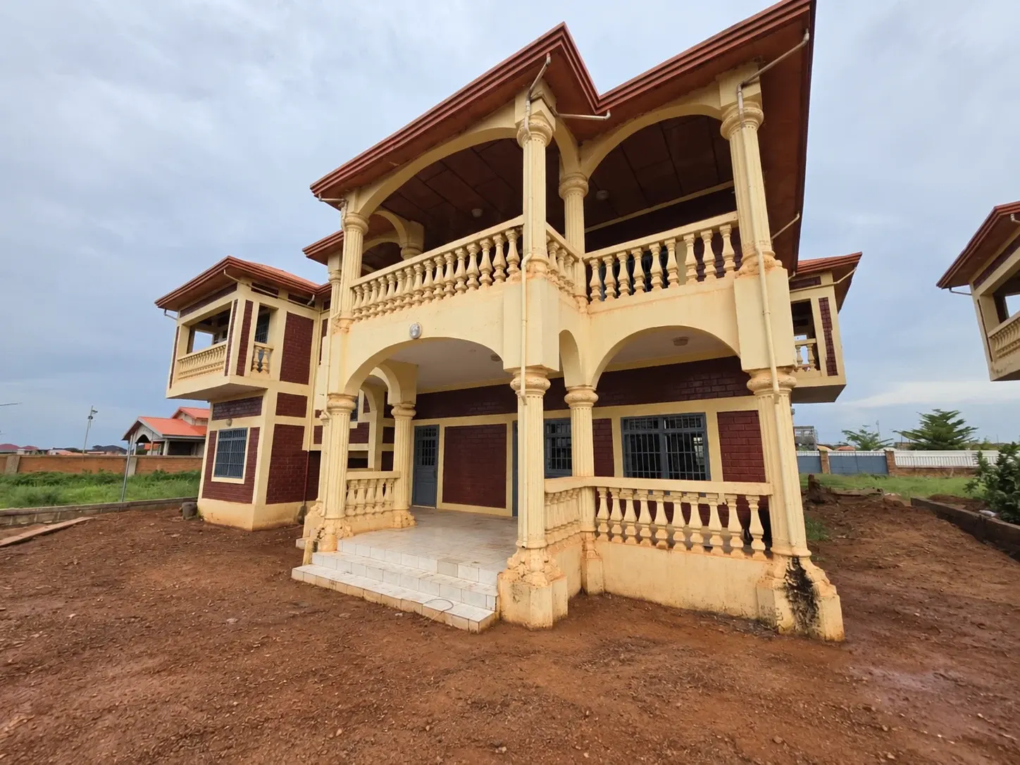Façade du duplex avec balcon, colonnes et entrée sur terrain en terre